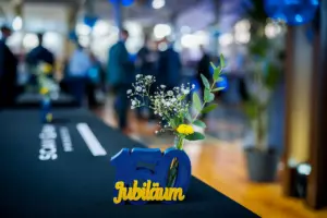 Jubiläumsaufsteller mit Blumen auf dem Tisch, Gäste unscharf im Hintergrund