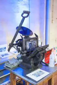 Historische Handpresse mit Druckform und Jubiläumsdrucken im blauen Licht